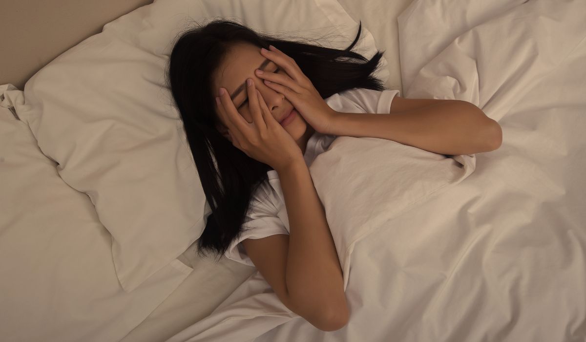 Mulher acordada na cama com as mãos no rosto, ilustrando a relação entre metabolismo e sono e os impactos de noites mal dormidas
