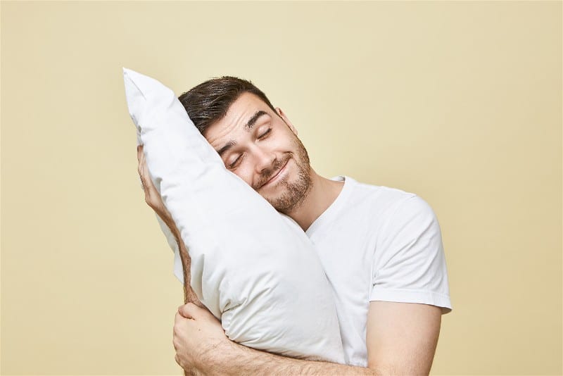 Homem abraçando um travesseiro com os olhos fechados