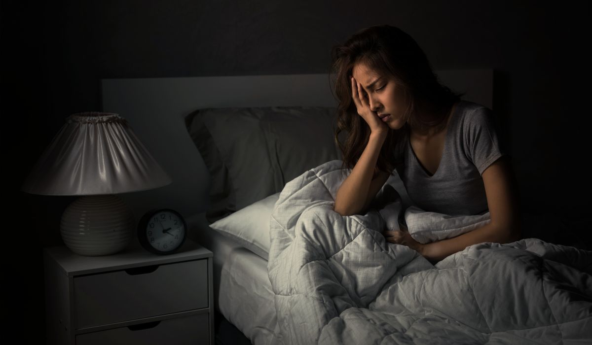 Mulher sentada na cama durante a noite com expressão de cansaço e dificuldade para dormir, representando o tema como dormir rapido insonia