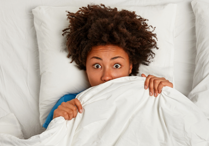mulher negra deitada na cama com pesadelo cobrindo o rosto