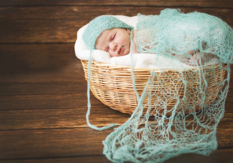 bebe recém nascido dormindo em uma cesta com panos azul em cima dele