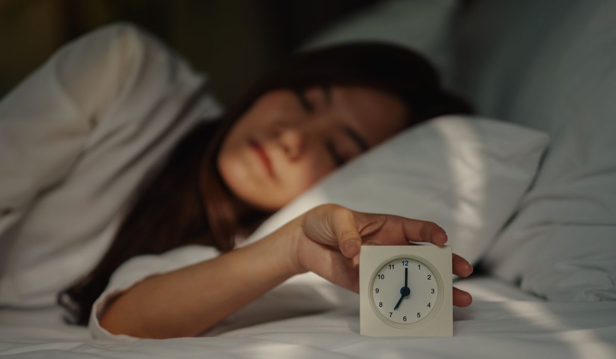 Pessoa deitada segurando um relógio na cama, ilustrando sono polifasico o que e e a divisão dos períodos de descanso