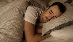 Homem dormindo de lado em cama confortável, ilustrando o tema sono profundo o que e e a importância do descanso reparador