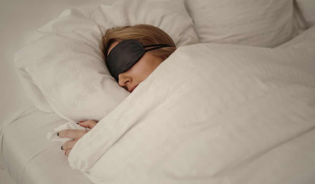 Mulher dormindo com máscara de descanso em cama confortável, ilustrando terapia do sono como funciona e cuidados para melhorar a qualidade do sono