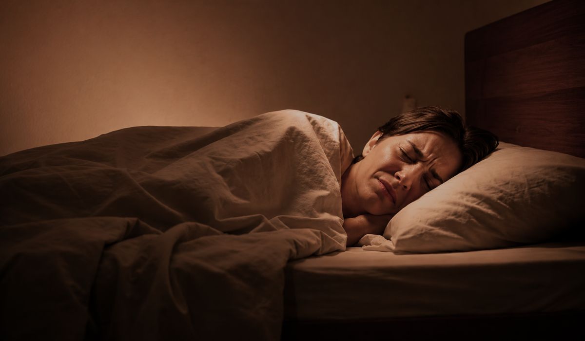 Mulher deitada na cama com expressão de medo e desconforto, ilustrando paralisia do sono e o que é esse fenômeno.
