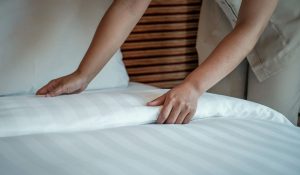 Pessoa ajustando lençol branco na cama, ilustrando dicas de como deixar a cama bonita, organizada e aconchegante