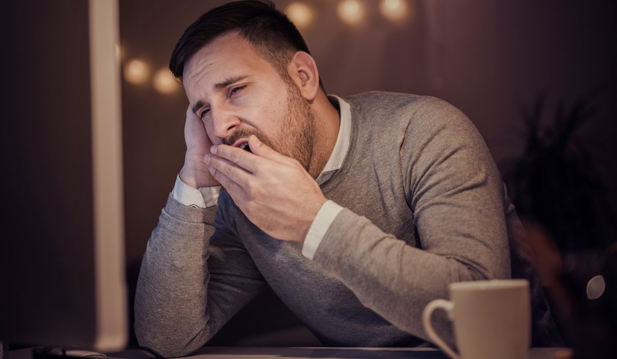 Homem bocejando com expressão de cansaço em ambiente interno, ilustrando para que serve o bocejo e sua relação com sono e sonolência