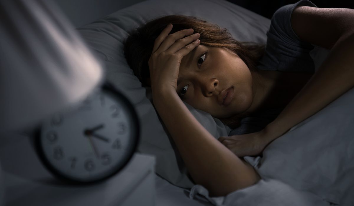Mulher acordada na cama durante a noite com expressão de preocupação, ilustrando falta de sono e o que fazer para dormir melhor