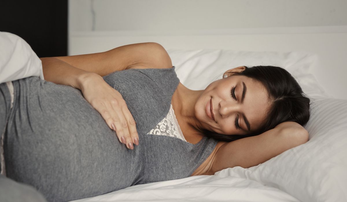 Mulher grávida dormindo de lado em cama confortável, ilustrando dicas de como dormir melhor na gravidez com mais conforto e segurança
