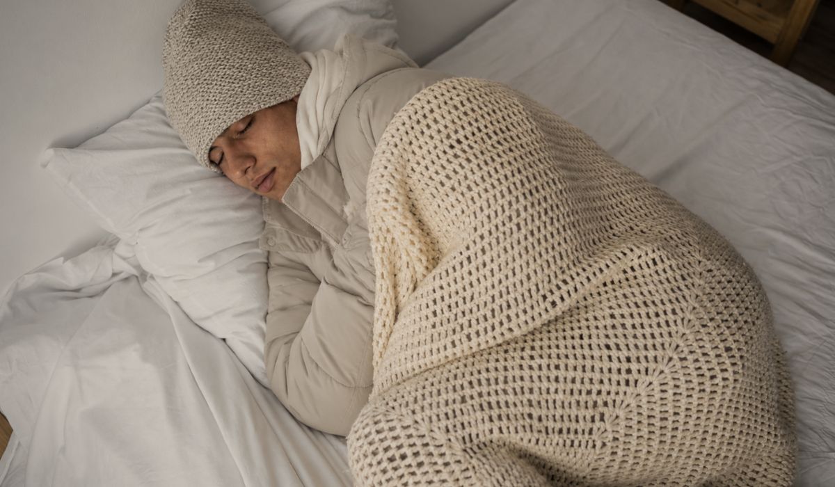 Pessoa dormindo coberta e agasalhada na cama, ilustrando por que sentimos mais sono no frio e como a temperatura influencia o descanso