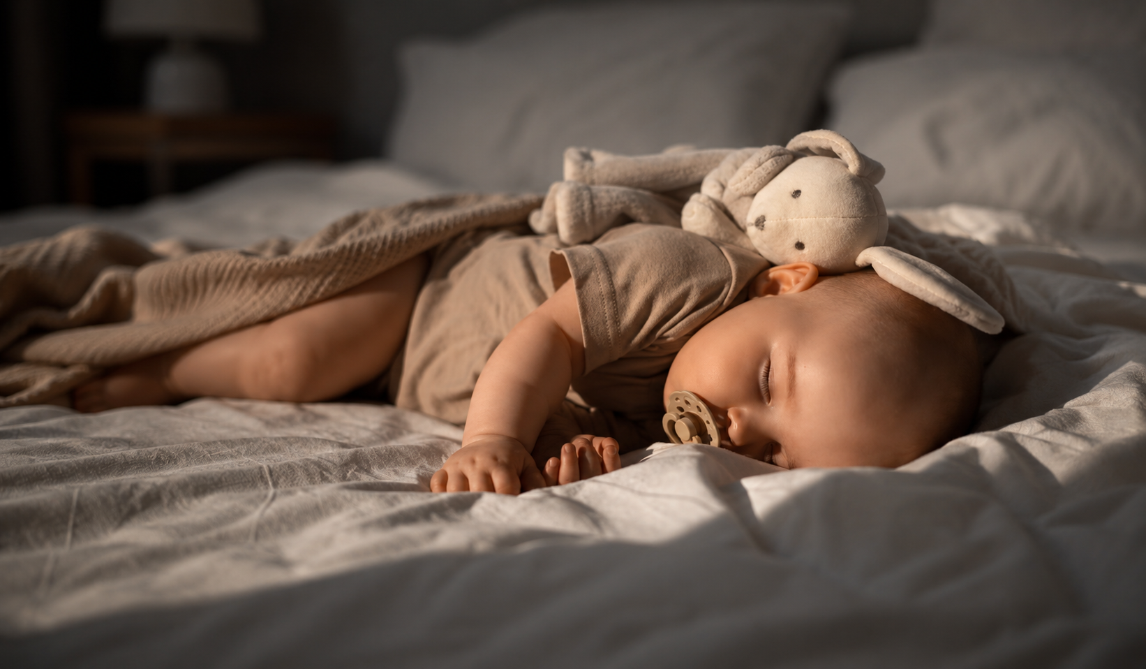 Bebê dormindo tranquilamente na cama com chupeta e bichinho de pelúcia, ilustrando o tema como fazer bebê dormir a noite toda