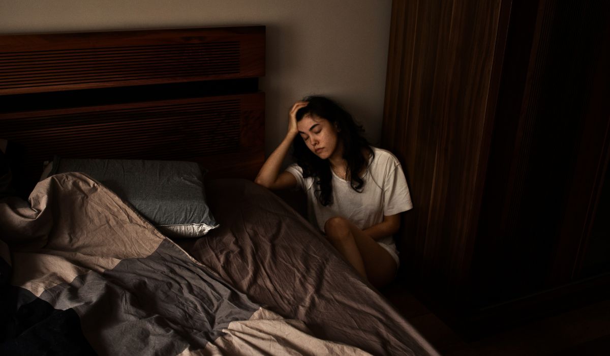 Mulher sentada ao lado da cama em um quarto escuro, com expressão de cansaço e desconforto, ilustrando o tema terror noturno e o que é esse distúrbio do sono