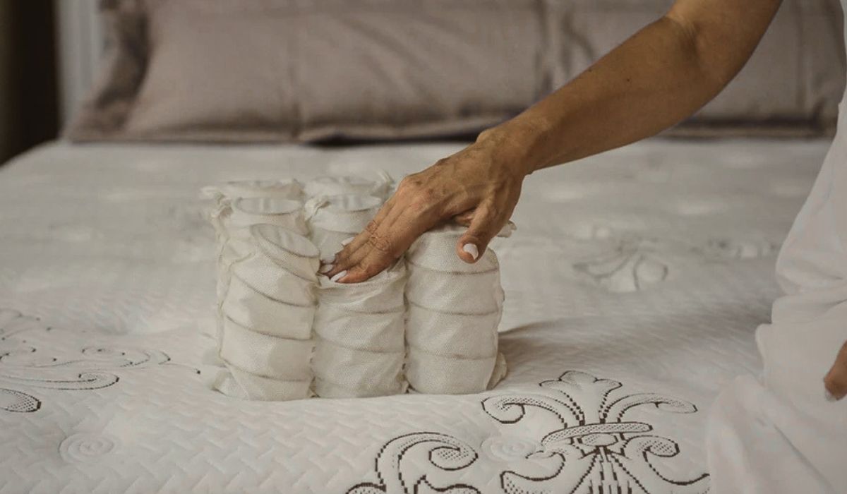 Mão pressionando conjunto de molas ensacadas sobre colchão, ilustrando os tipos de molas de colchao e suas diferenças no conforto