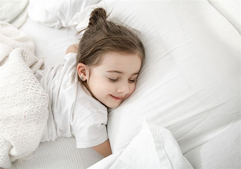 criança dormindo em um colchão com lençóis branco