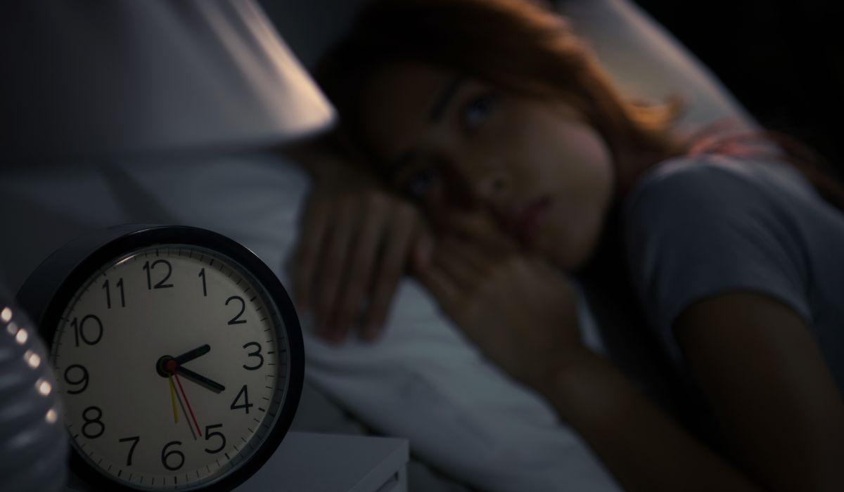 Mulher acordada de madrugada na cama olhando para o relógio, ilustrando dificuldade para voltar a dormir durante a noite
