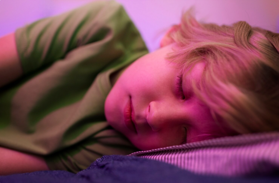 Criança dormindo com iluminação rosa no quarto, ilustrando cromoterapia cores para dormir e a influência das luzes no sono