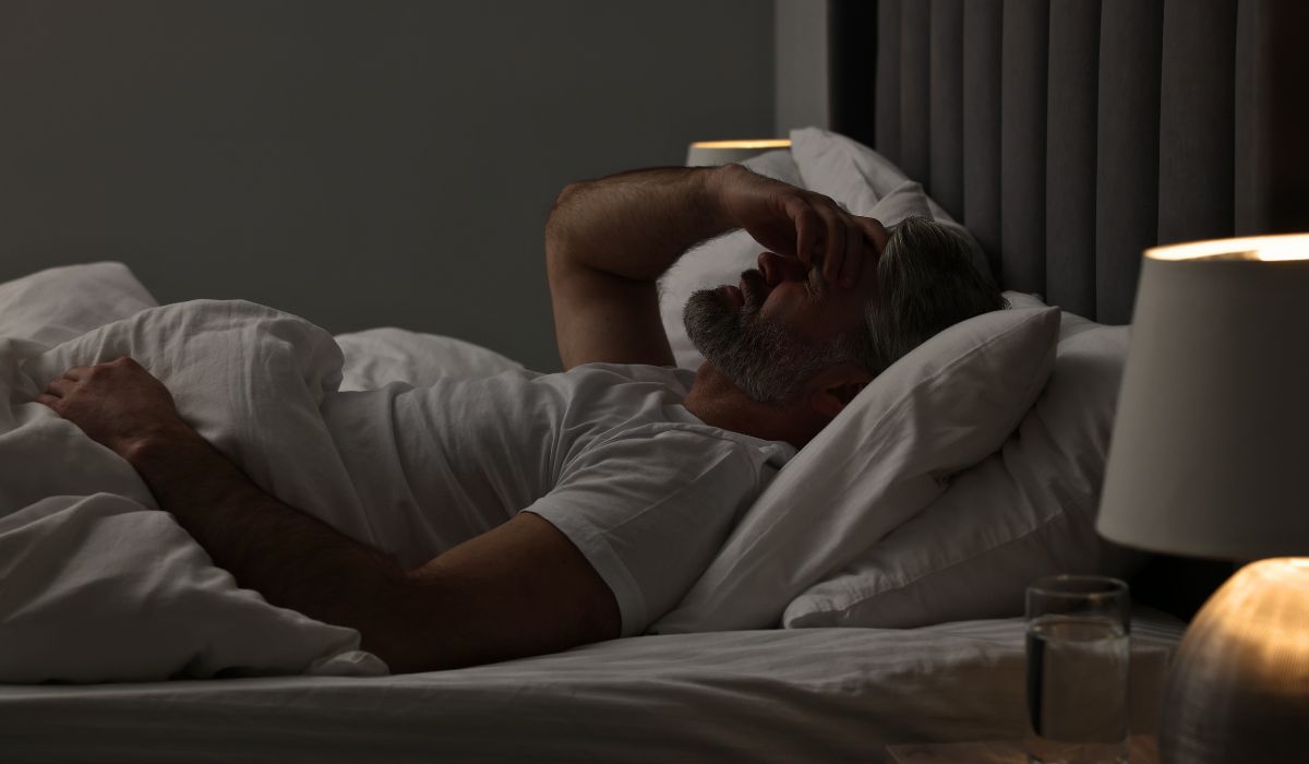 Homem acordado de madrugada na cama com expressão de cansaço, ilustrando insônia e dificuldade para voltar a dormir.