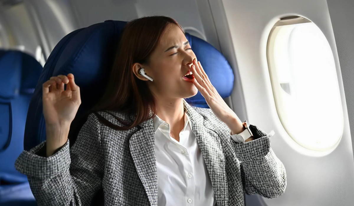 Mulher bocejando dentro de um avião, ilustrando jet lag, cansaço em viagens longas e como tratar a alteração do sono.