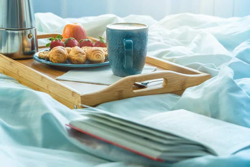 Bandeja de bambu com croissant, morango e leite em cima da cama