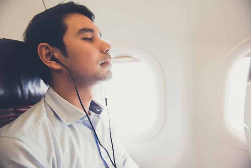 Homem com os olhos fechados escutando música no fone dentro de um avião