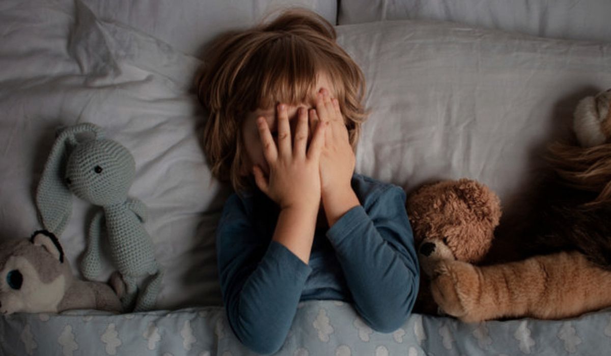 Criança na cama cobrindo o rosto com as mãos, ilustrando espasmo infantil durante o sono e alterações no descanso infantil.