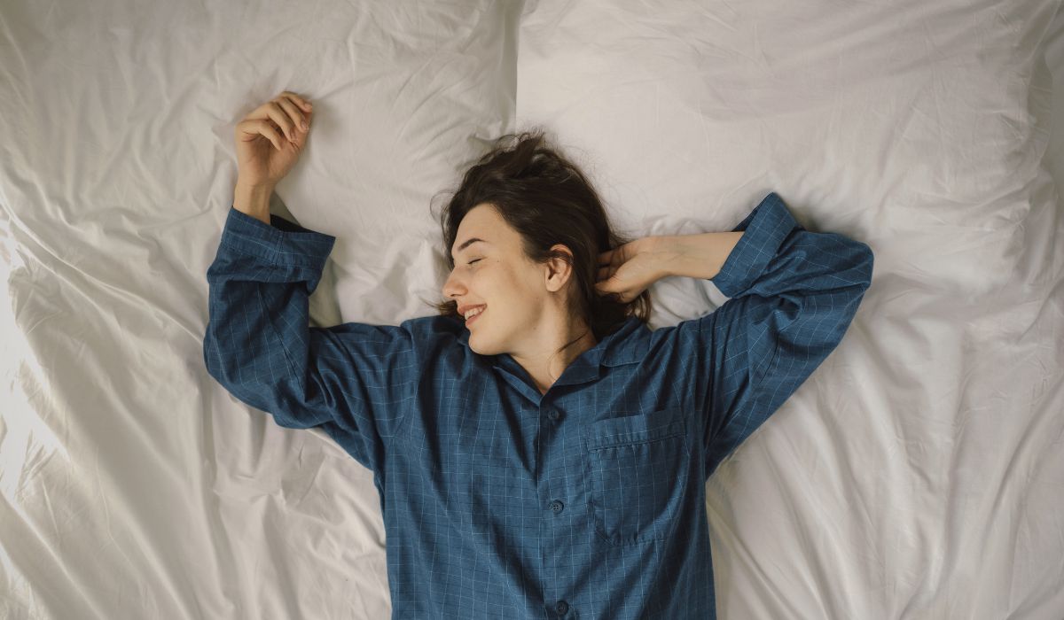 Mulher de pijama sorrindo e relaxada sobre a cama, representando conforto e o colchão ideal para uma boa noite de sono.