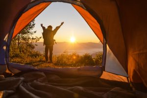 Homem com braços abertos diante do nascer do sol em acampamento