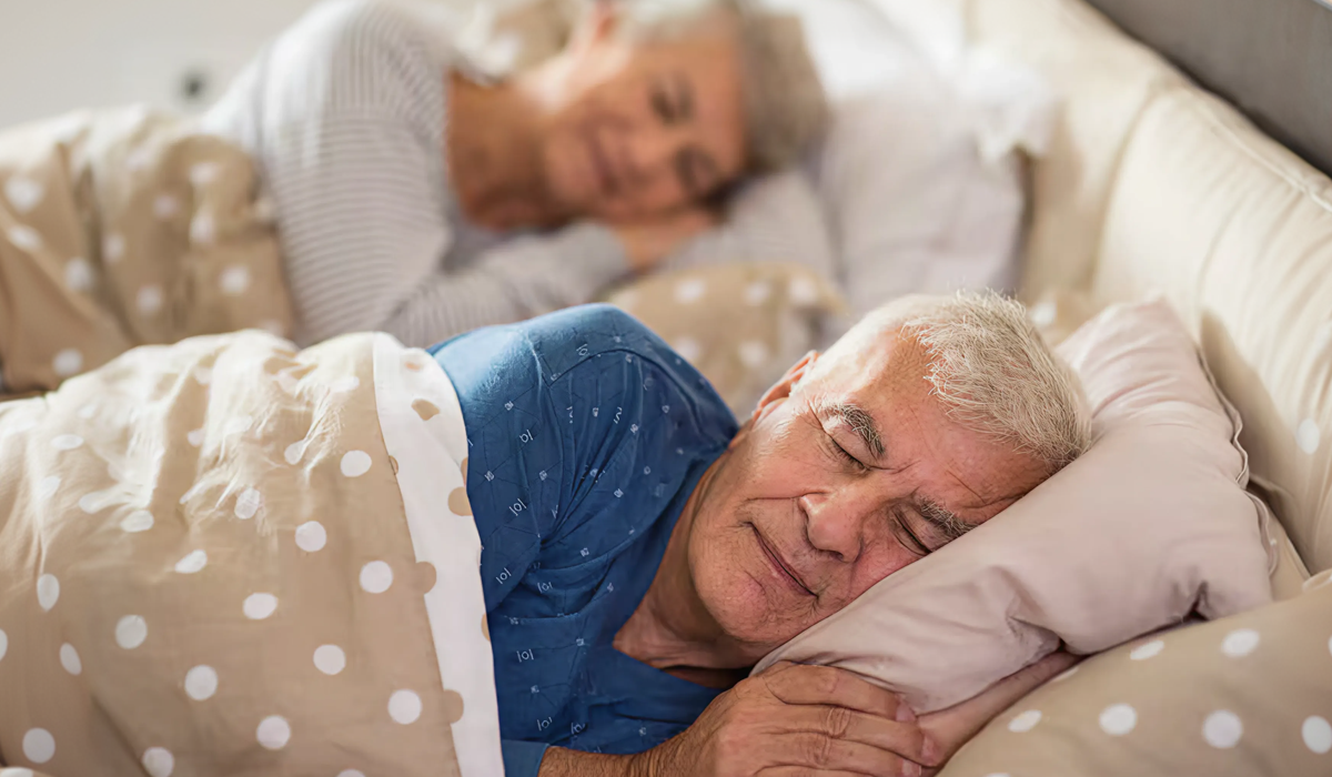 Casal de idosos dormindo tranquilamente na cama, ilustrando o sono na terceira idade e a importância do conforto para descansar melhor.