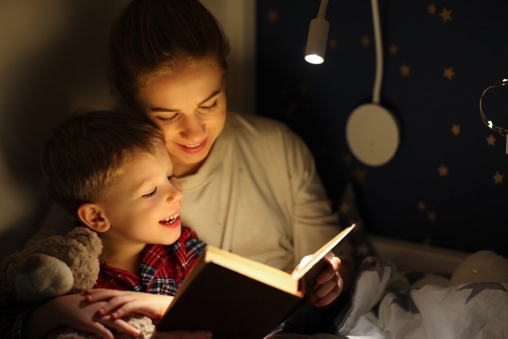 Mãe lendo uma história para seu filho antes de dormir, ambos sorrindo em um ambiente aconchegante com luz suave.