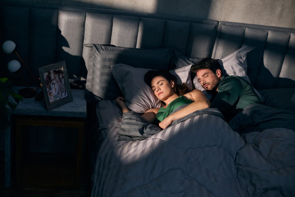 Casal dormindo confortavelmente em colchão e travesseiros de viscoelástica, com alinhamento do corpo e ambiente elegante de quarto