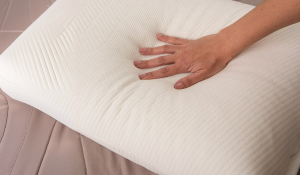 Mão pressionando um travesseiro branco, destacando o conforto e a adaptação dos travesseiros de látex