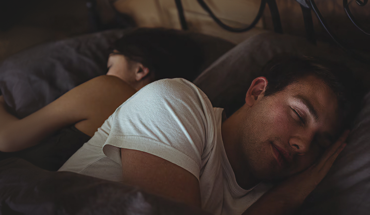 Casal dormindo na mesma cama, de costas um para o outro, ilustrando conforto, descanso e qualidade do sono a dois.