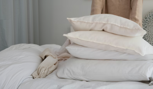 Pessoa organizando travesseiros brancos sobre a cama, representando conforto, higiene e a importância de escolher o travesseiro ideal