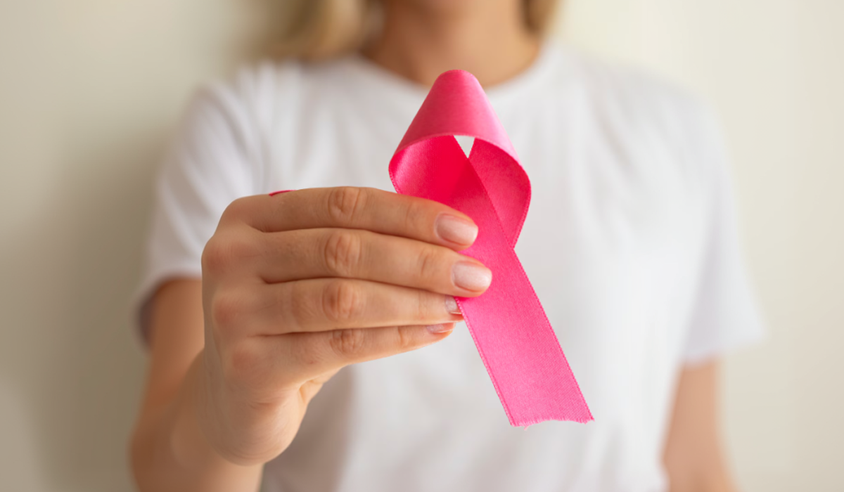 Pessoa segurando laço rosa de conscientização, representando a relação entre sono e saúde da mulher, autocuidado e prevenção.